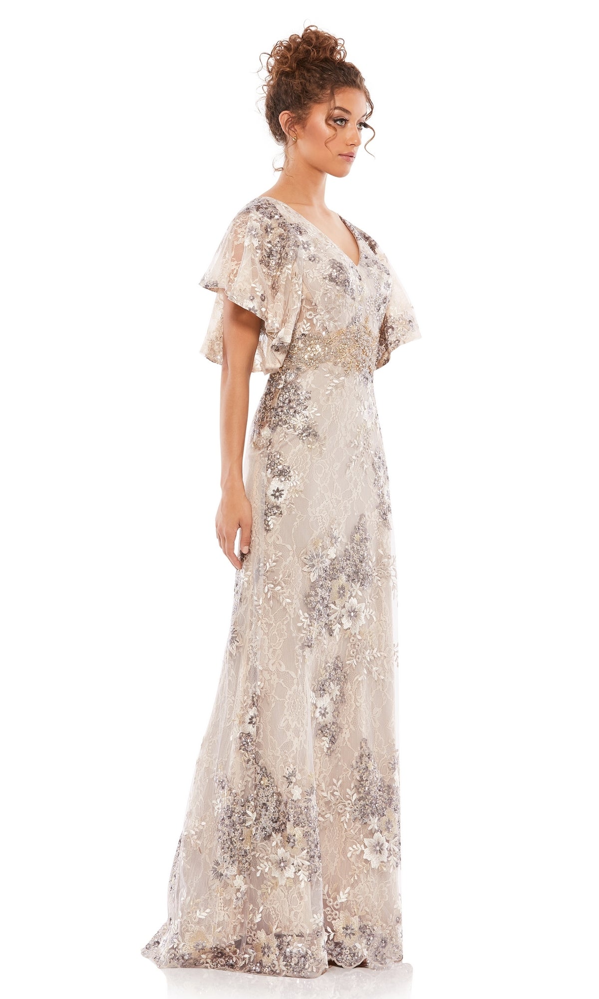 A woman stands in profile wearing the Mac Duggal 67842 Flutter-Sleeve Long Formal Dress, featuring short flutter sleeves, a V-neck, a floor-length skirt, light lace overlay, and delicate floral embellishments.